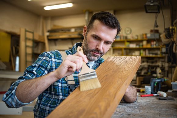 Mann lackiert ein Holzbrett